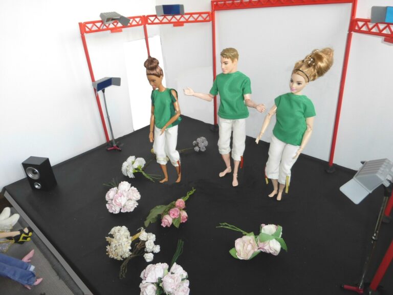 3 dolls onstage with flowers on black floor